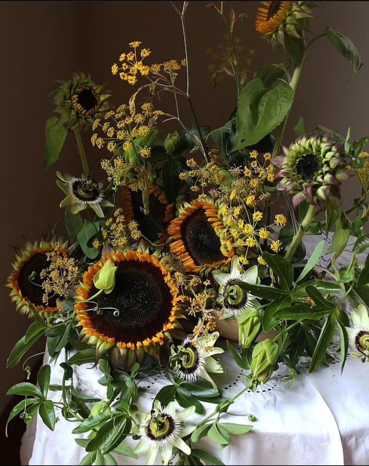 an arrangement of sunflowers and other flowers in a vase on a white cloth