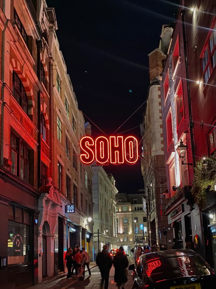 the neon sign says soho above an alleyway with cars parked on both sides