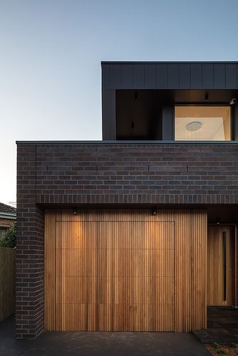 a brick house with wooden garage doors and plants on the top of it's roof