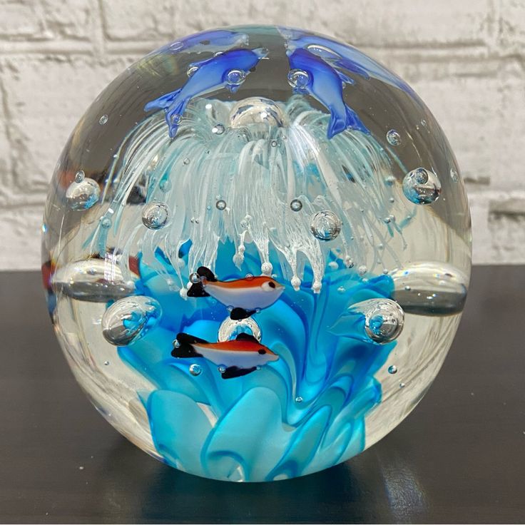 a glass bowl with two fish in it on a black table next to a brick wall