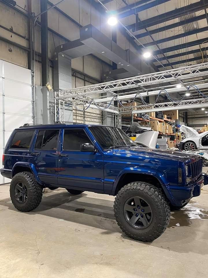 a blue jeep is parked in a garage with other vehicles behind it and on the ground