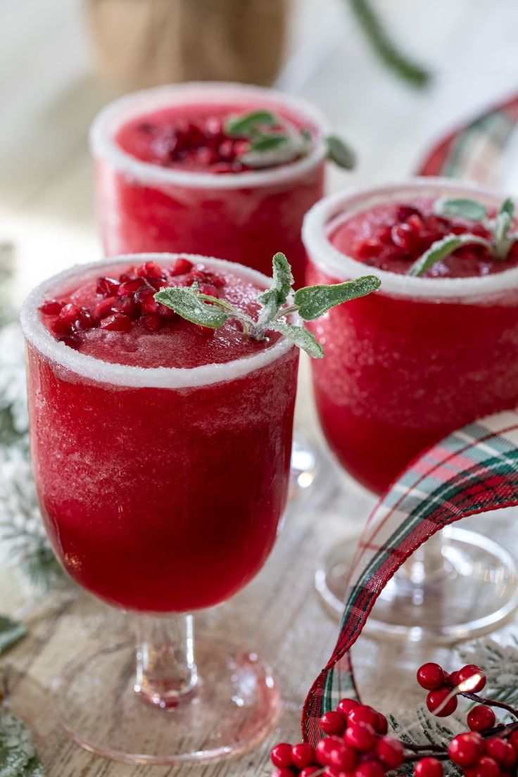 three glasses filled with red liquid and garnished with holly