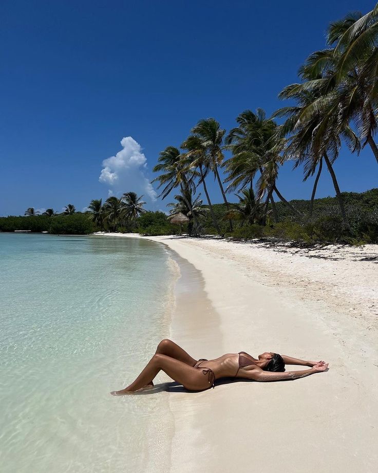 a woman laying on the beach with palm trees in the backgroung and clear water