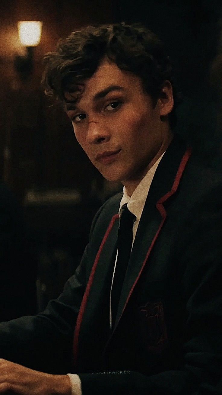 a young man wearing a suit and tie sitting at a table with a laptop in front of him