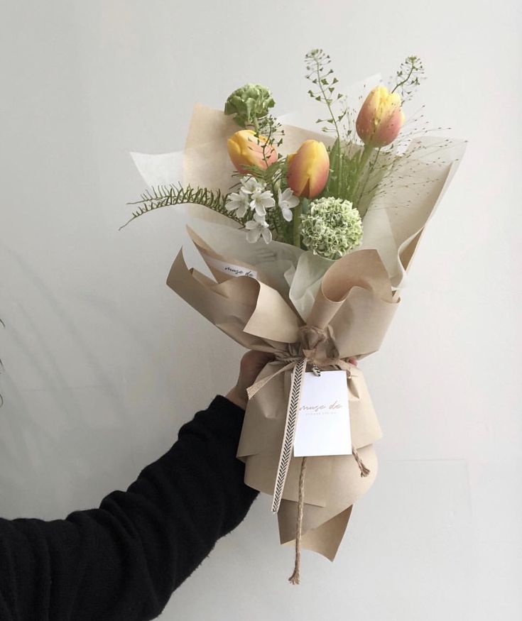 a person holding a bouquet of flowers in front of a white wall with a tag on it