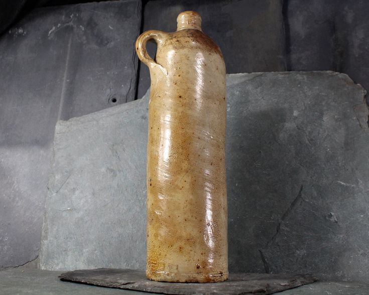 a brown jug sitting on top of a stone slab next to a gray rock wall