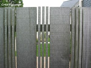 a wooden fence with metal posts in front of a house and grass area behind it