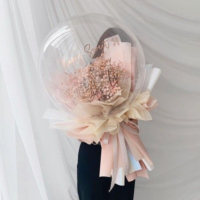 there is a large balloon with flowers in it on the table next to a white curtain