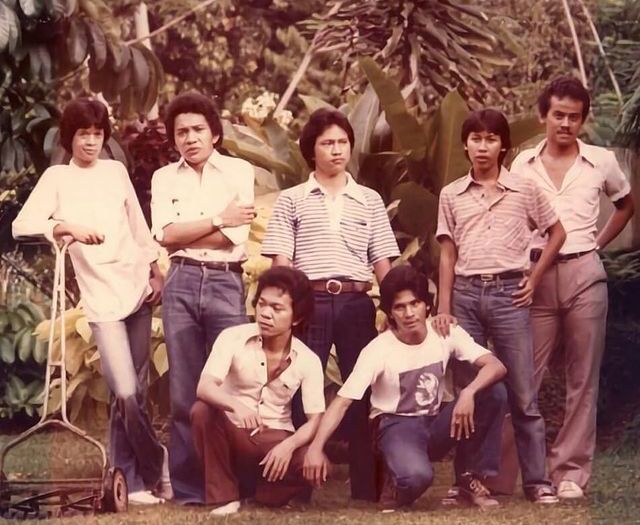 a group of people standing next to each other in front of some trees and bushes