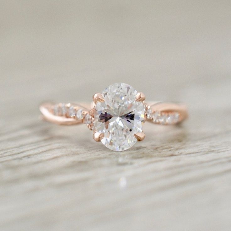 a close up view of a diamond engagement ring on a wooden surface with the center stone set in 18k rose gold