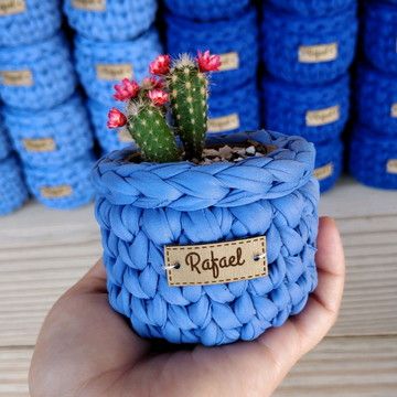 a hand holding a small blue basket with a cactus in it and several stacks of blue yarn behind it