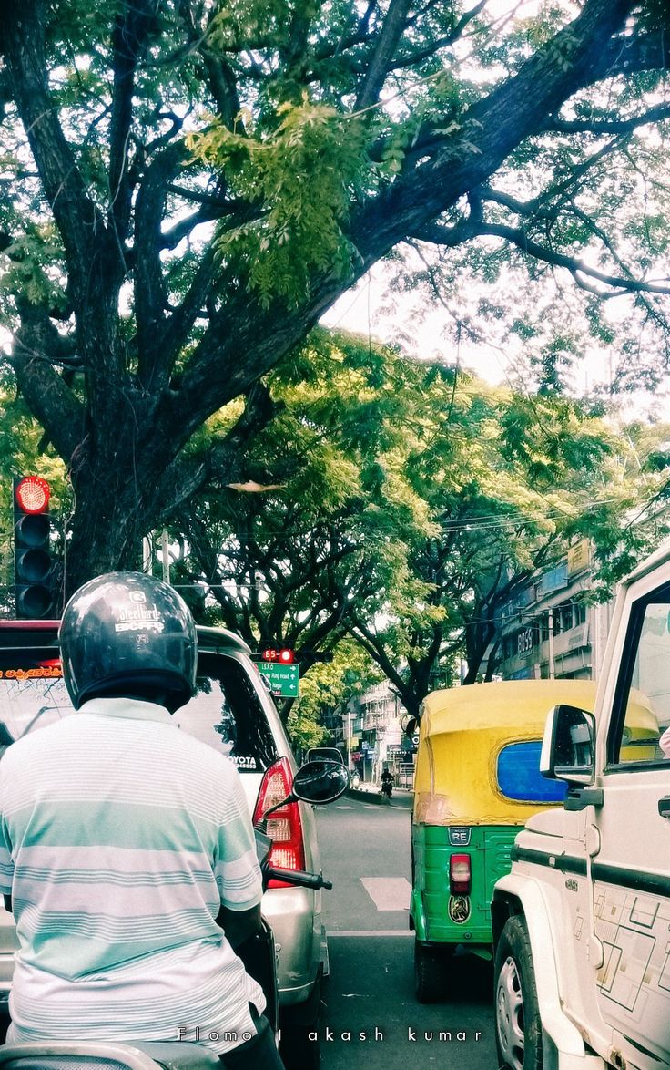 a man riding a motorcycle down a street next to parked cars and trees in the background