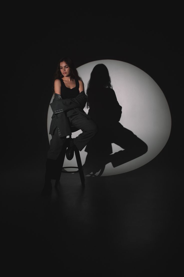 a woman sitting in a chair with her shadow on the wall behind her as she poses for a photo