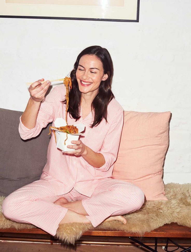 a woman sitting on a couch holding a bowl of food in her hand and smiling