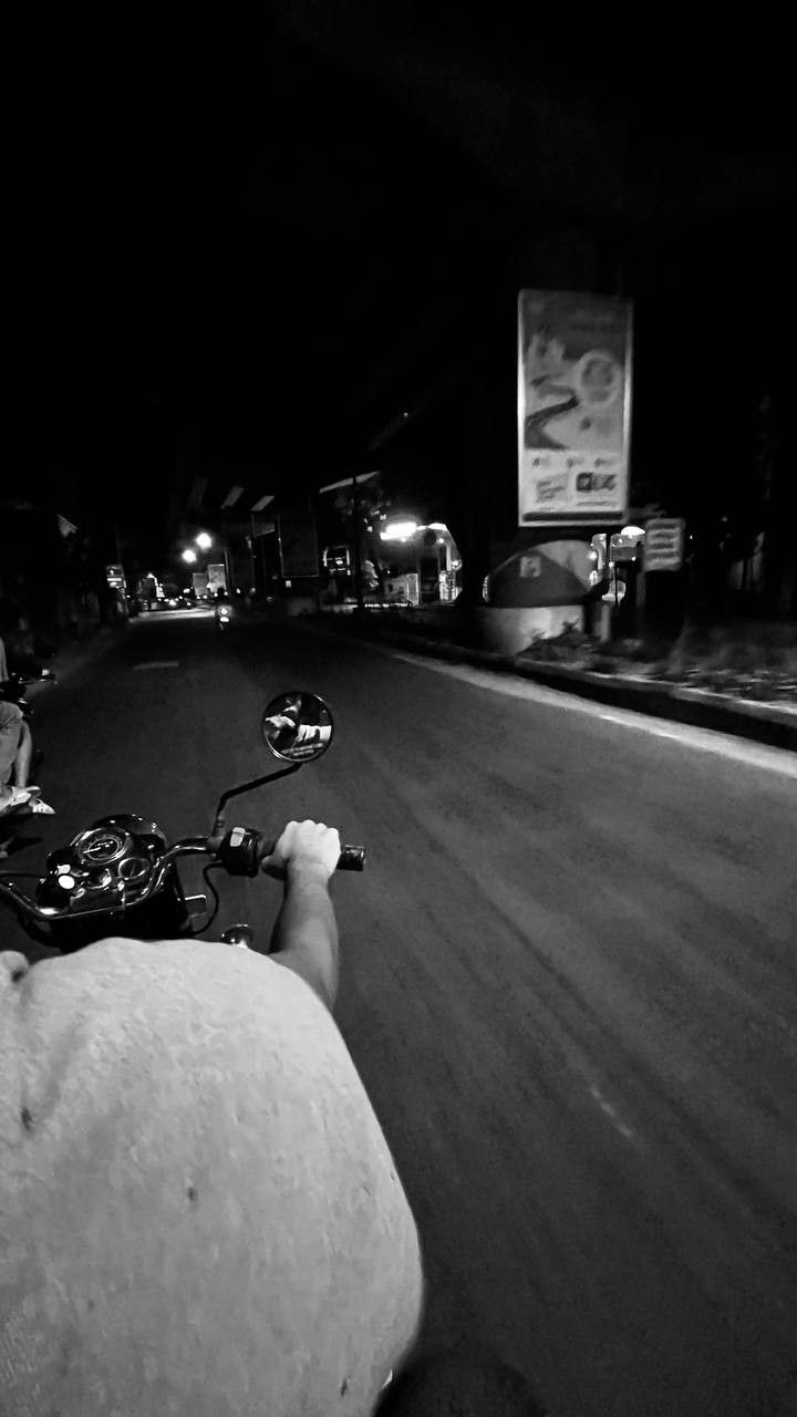 two people riding on the back of motorcycles at night in black and whit photo