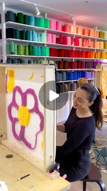 a woman sitting in front of a painting with flowers on it and spools of thread