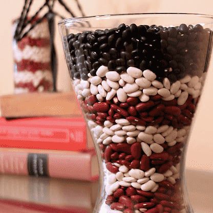 a glass vase filled with beans and other things on top of a table next to a stack of books