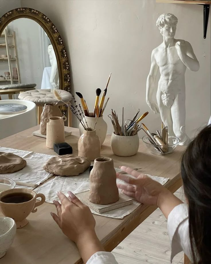 a woman sitting at a table working on clay art work with her hands in the air