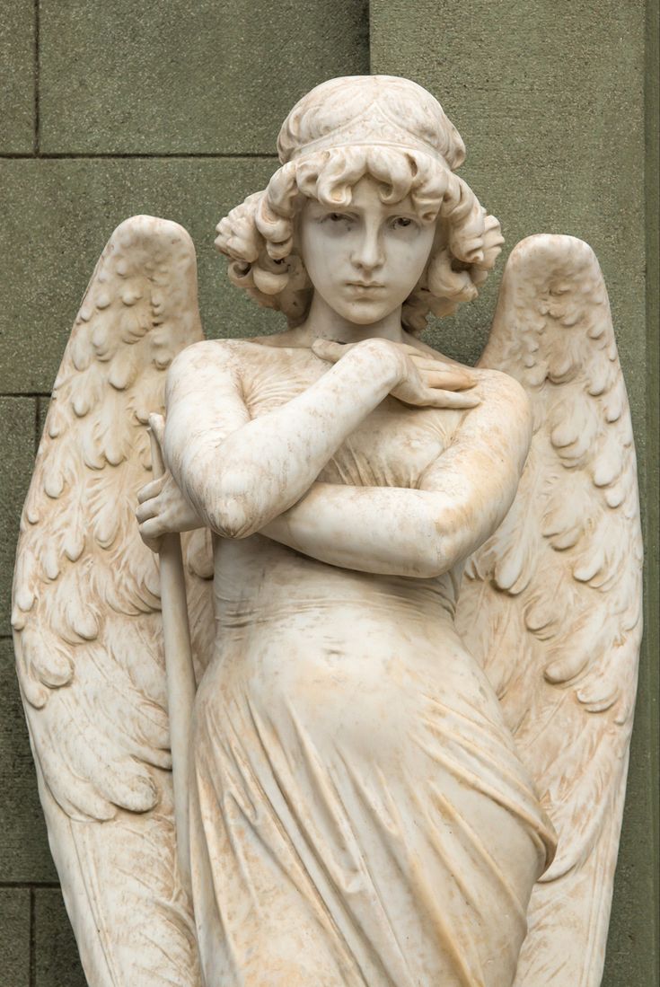 an angel statue is standing in front of a building with its arms crossed and hands folded