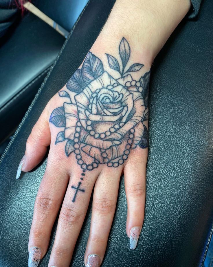 a woman's hand with a cross and rose tattoo on the middle of it