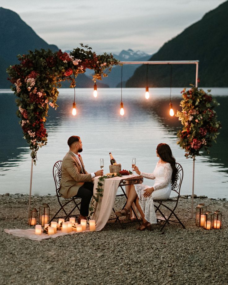 a man and woman sitting at a table next to each other with candles on the ground