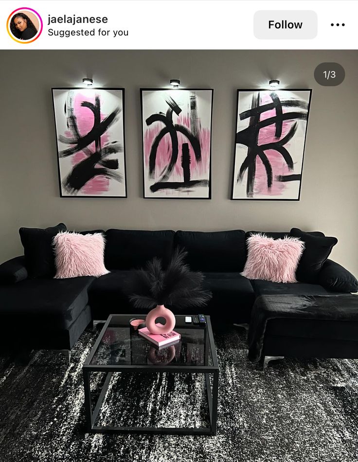 a living room with black couches and pink pillows on the wall, two framed pictures above them