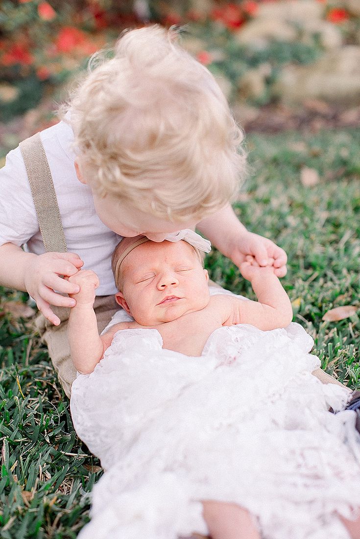 a baby in a white dress is playing with another baby on the grass and looking at her