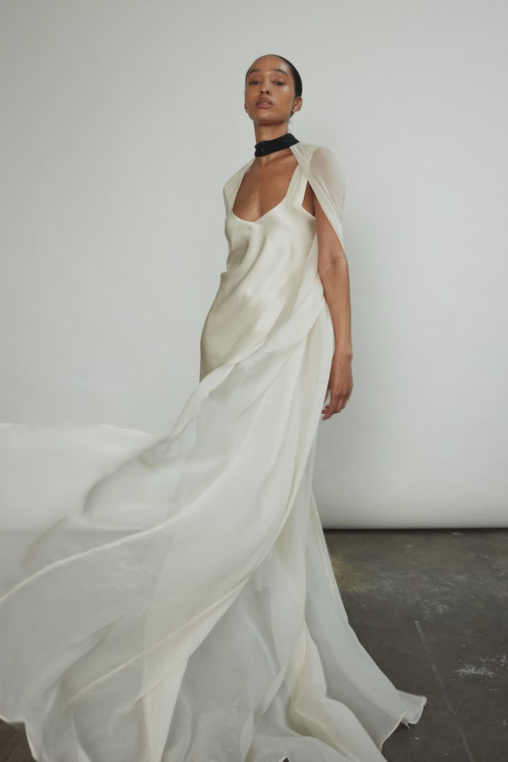 a woman wearing a white dress and black choker standing in front of a white wall