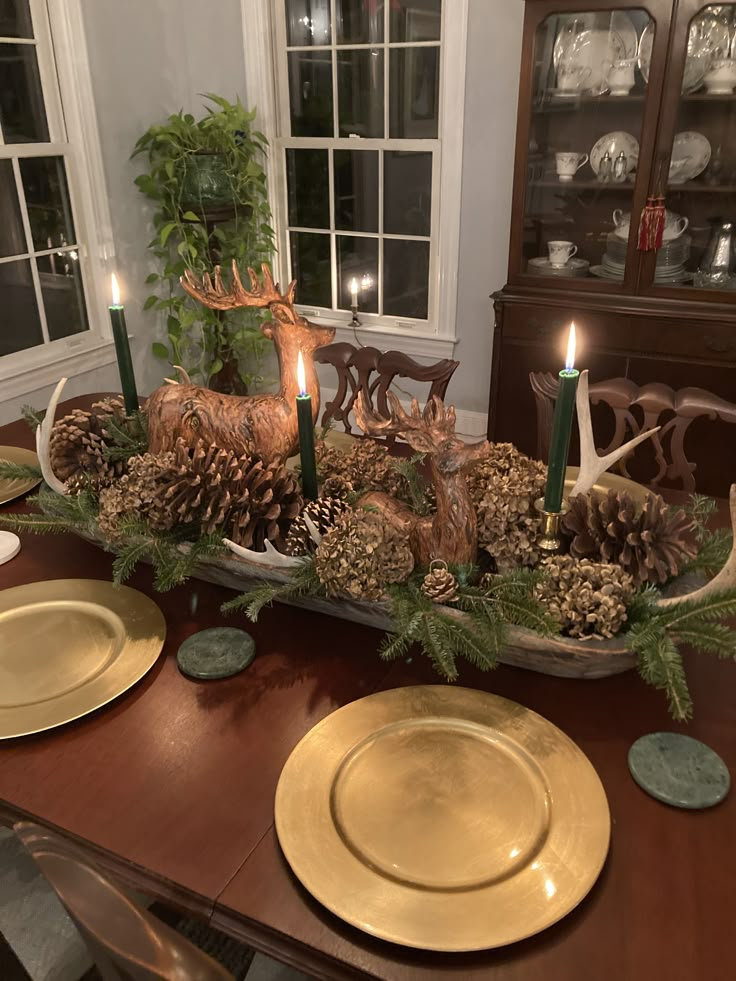 a dining room table decorated with pine cones, evergreens and deer antlers for the centerpiece