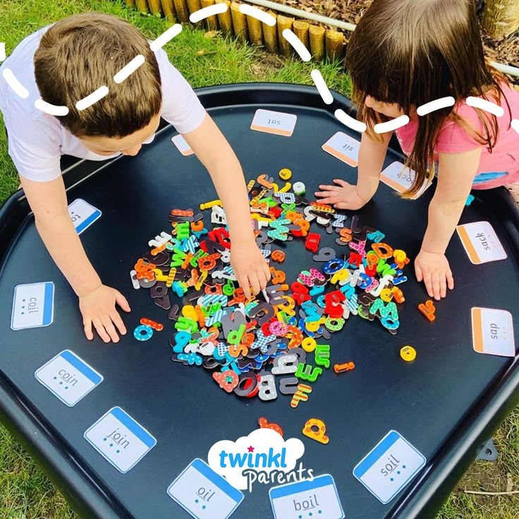 two young children playing with letters and numbers on a play table in the grass outside