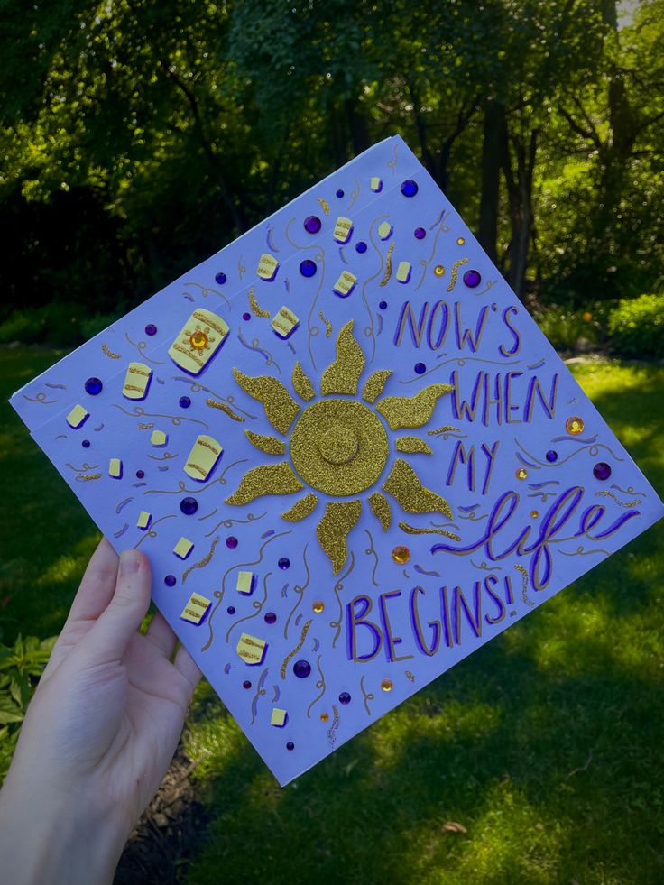 someone holding up a purple and gold graduation cap with the words now's when my life begins