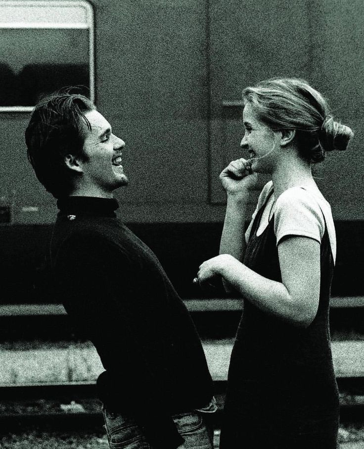 black and white photograph of two people standing next to each other on train tracks eating donuts