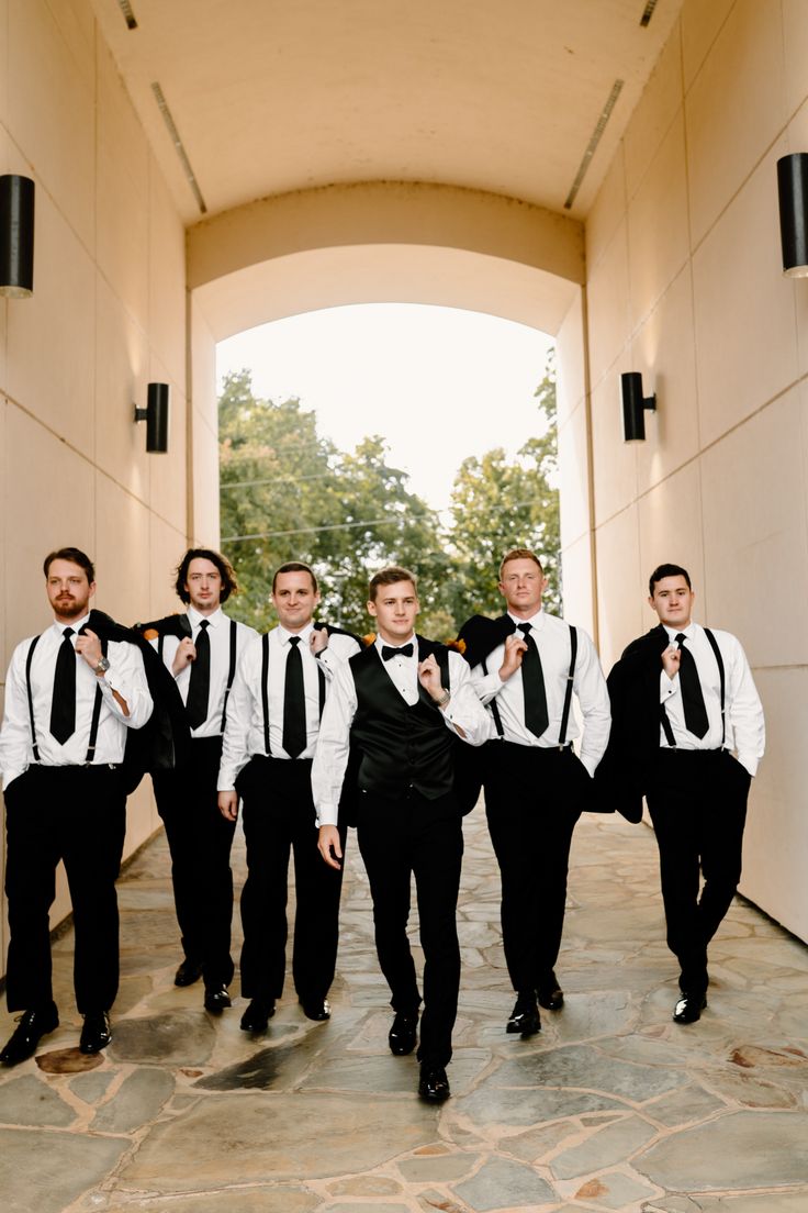 a group of men in black and white suits walking down a hallway with their arms around each other