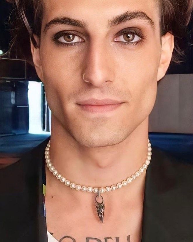 a man wearing a necklace with pearls and a cross on the front is looking at the camera