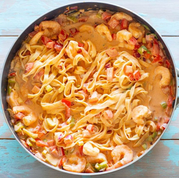 a pan filled with pasta and shrimp on top of a wooden table