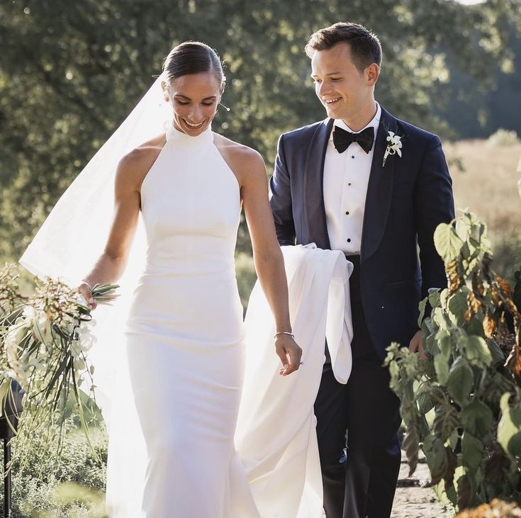 a bride and groom walking down a path holding each other's hands as they look at each other