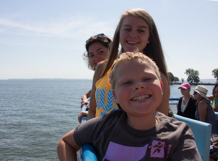 two girls and a boy on a boat in the water with people watching from behind them