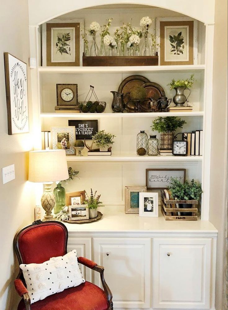 a red chair sitting in front of a white book shelf filled with books and plants