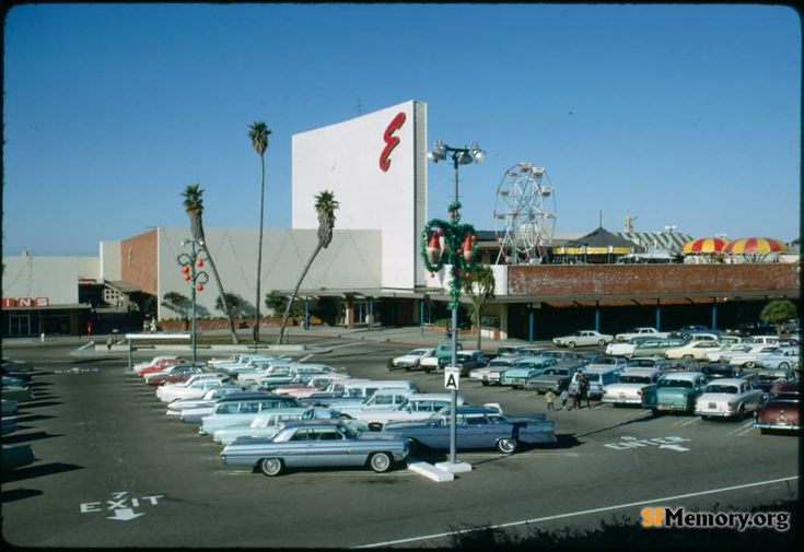 a parking lot with cars parked in front of a building and ferris wheel behind it