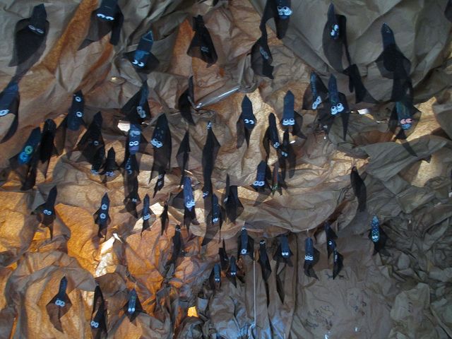 there are many small black birds perched on the rock wall and hanging from it's sides