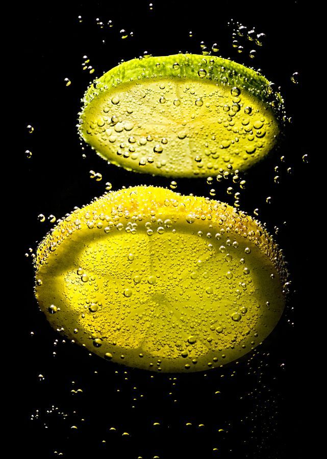 three slices of lemon with water droplets on the black backgrounnd, one is yellow and the other is green