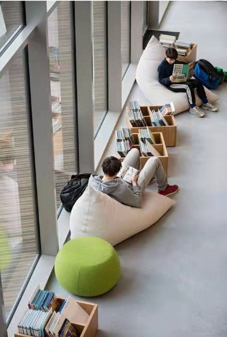 two people sitting on bean bag chairs reading books in the library with their backs to each other