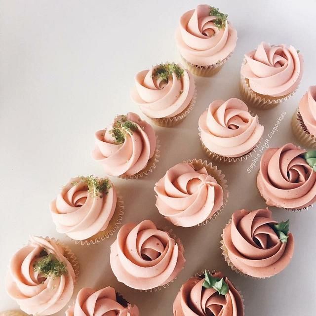 several cupcakes with pink frosting and green leaves on top are arranged in a triangle