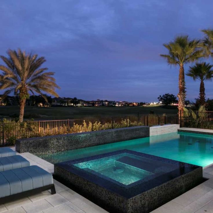 an outdoor swimming pool with lounge chairs and palm trees in the background at night time