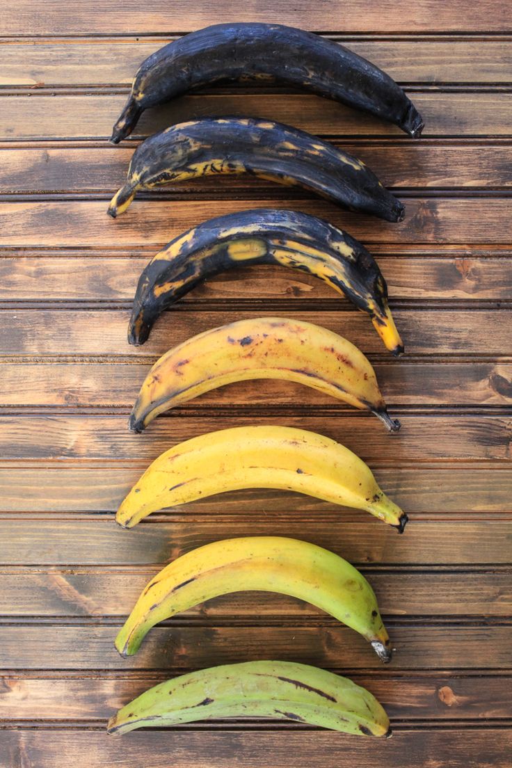 five different types of bananas lined up in a row on a wooden surface with one banana peeled and the other unripe