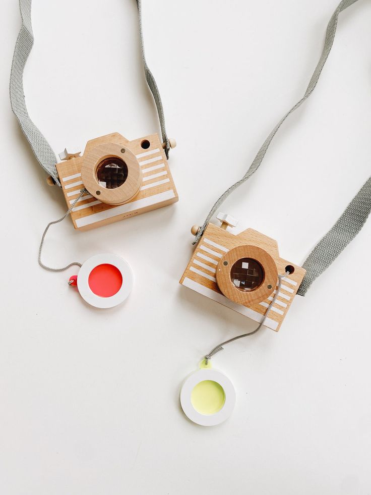 two wooden cameras sitting next to each other on a white surface with grey straps and an object in the foreground