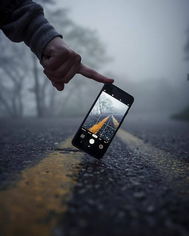 a person pointing at an image on their cell phone in the middle of the road