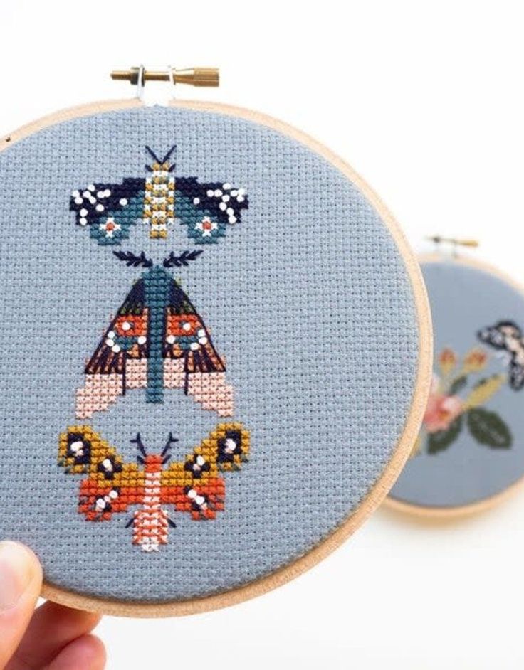 two cross - stitch kits are being held up in front of each other to show the finished designs