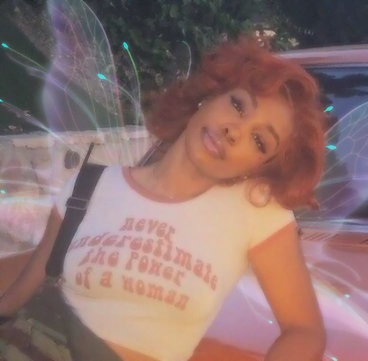 a woman with red hair is posing in front of a pink car and fairy wings