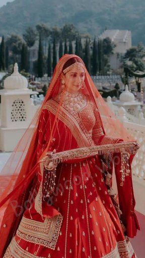 a woman in a red and gold bridal gown is standing on a balcony with mountains in the background